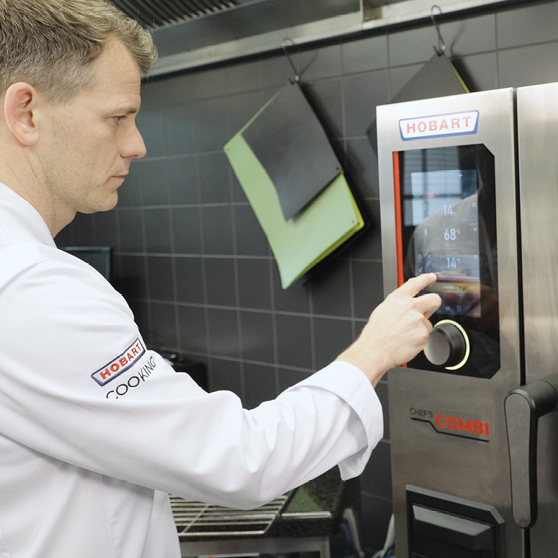 Kucharz obsługujący panel dotykowy urządzenia HOBART CHEF’S COMBI w profesjonalnej kuchni, dostosowując ustawienia do precyzyjnego gotowania.