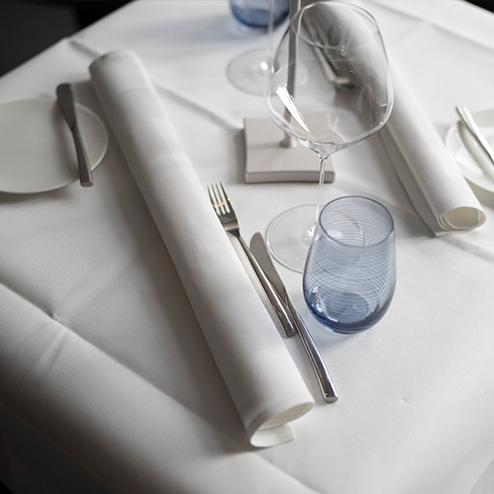 Elegancko nakryty stół restauracyjny z uporządkowanymi sztućcami, kieliszkami do wina, zwiniętymi serwetkami i niebieską szklanką, tworzący wyrafinowaną atmosferę.