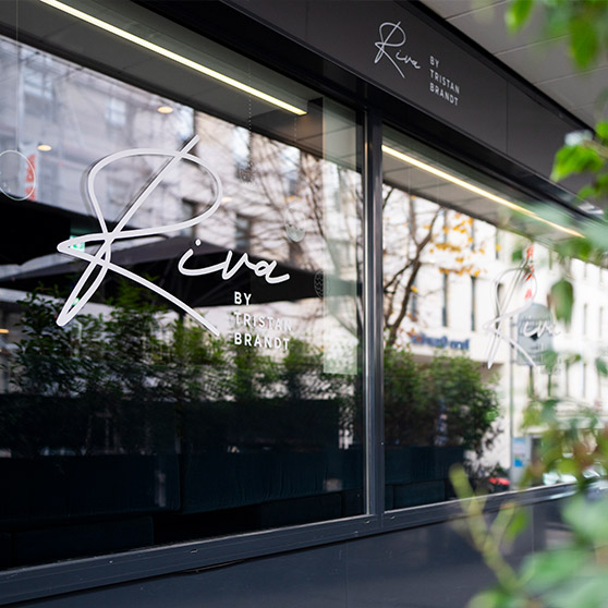 Widok zewnętrzny restauracji RIVA by Tristan Brandt w Pforzheim z charakterystycznym logo na dużych oknach.
